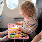 Child exploring a pink busy board activity book during a flight